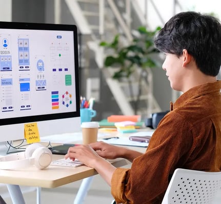 Une personne travaille sur un ordinateur et conçoit des prototypes d'interface utilisateur, entourée de papier à lettres coloré et d'une tasse de café.
