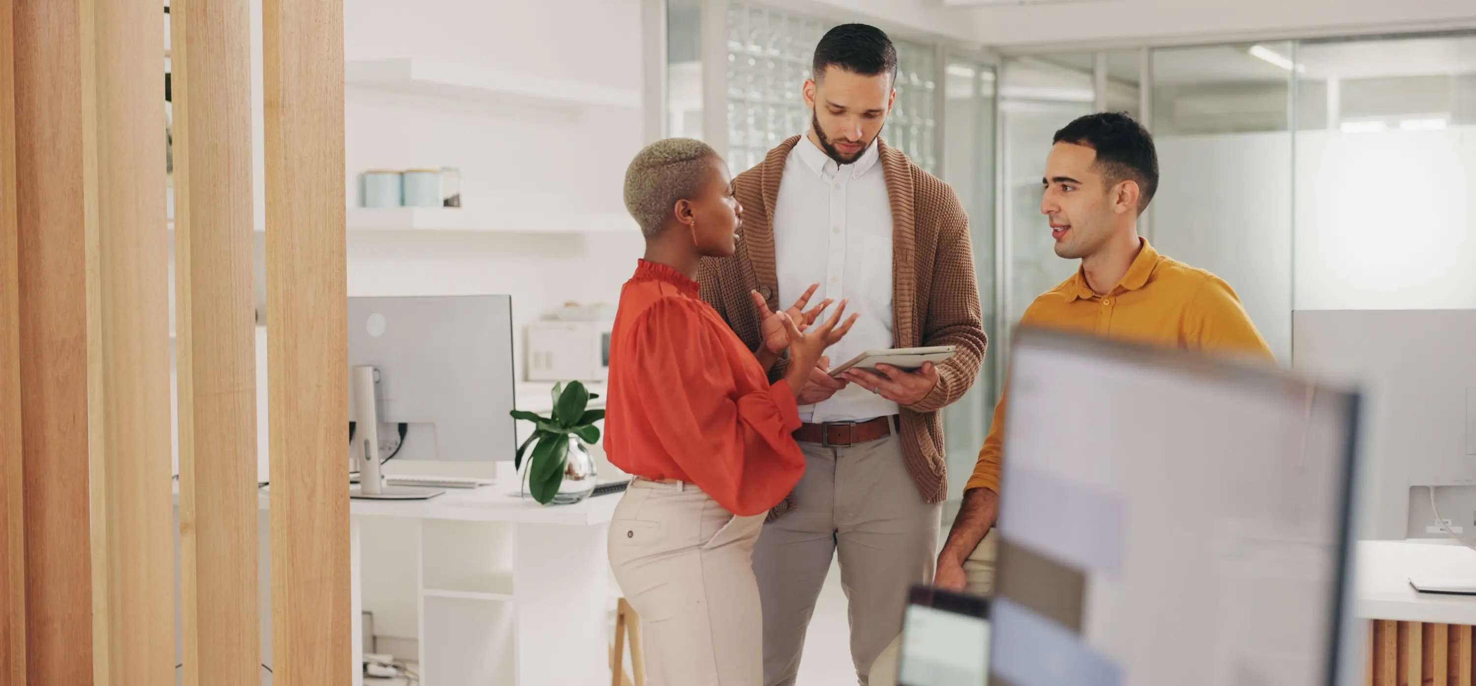 Trois collègues se livrent à une discussion animée sur l'accompagnement et la formation en marketing numérique dans un bureau moderne, entouré de plantes et d'un décor contemporain.