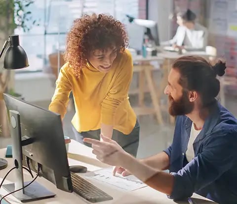 Two colleagues collaborate in a modern workspace, discussing a document amidst plants and office equipment.