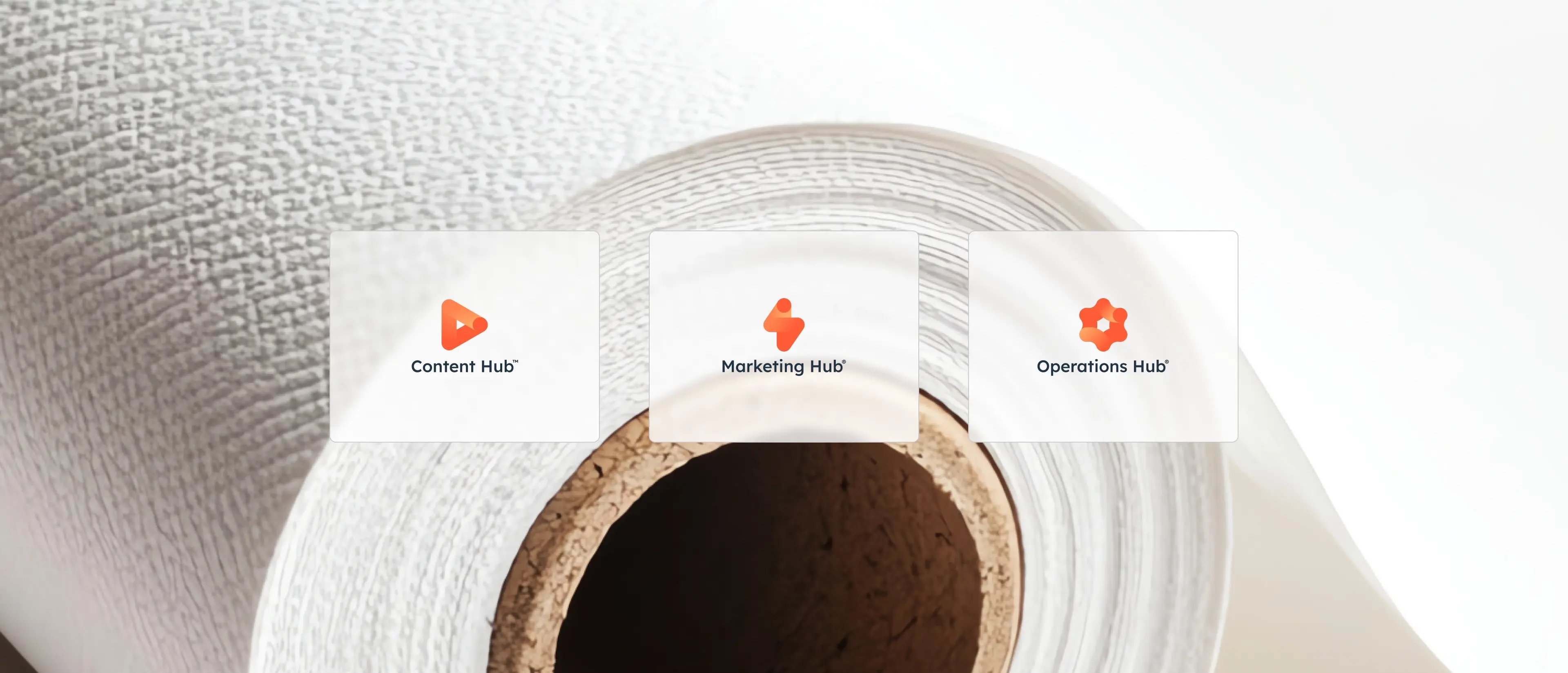 Trois icônes de hub de HubSpot : Content Hub, Marketing Hub et Operations Hub sont affichées sur un fond texturé de papier blanc.