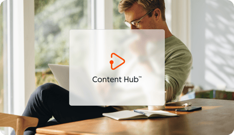 Une icônes de hub de HubSpot : Content Hub, est affichée sur une image d'une personne assise à une table en bois, travaillant sur un ordinateur portable entourée de verdure et de lumière naturelle.