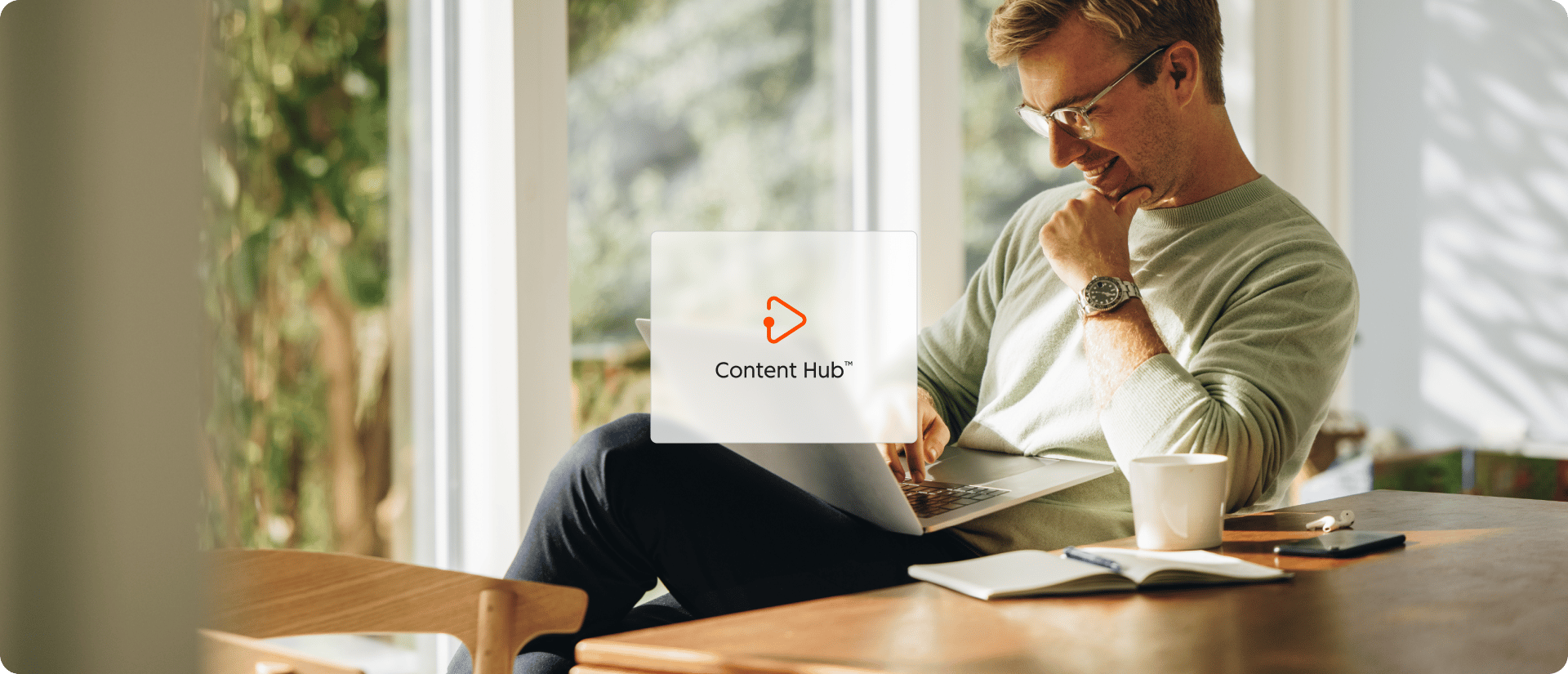 Une icônes de hub de HubSpot : Content Hub, est affichée sur une image d'une personne assise à une table en bois, travaillant sur un ordinateur portable entourée de verdure et de lumière naturelle.