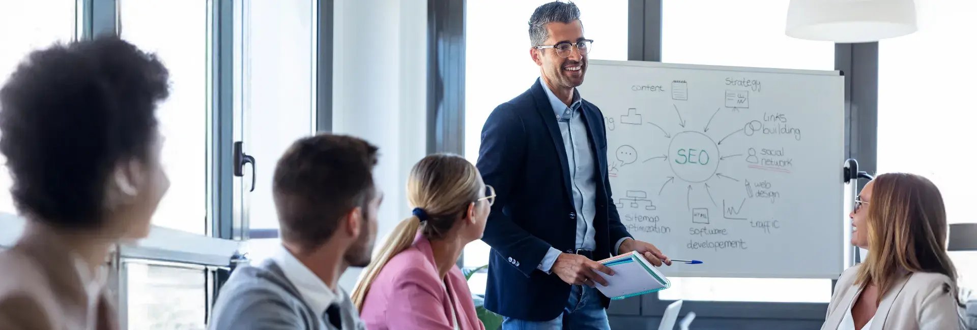 Un professionnel faisant une présentation sur les stratégies de référencement naturel (SEO), avec un tableau blanc sur lequel sont inscrits les concepts clés, tandis qu'un public attentif écoute avec intérêt.