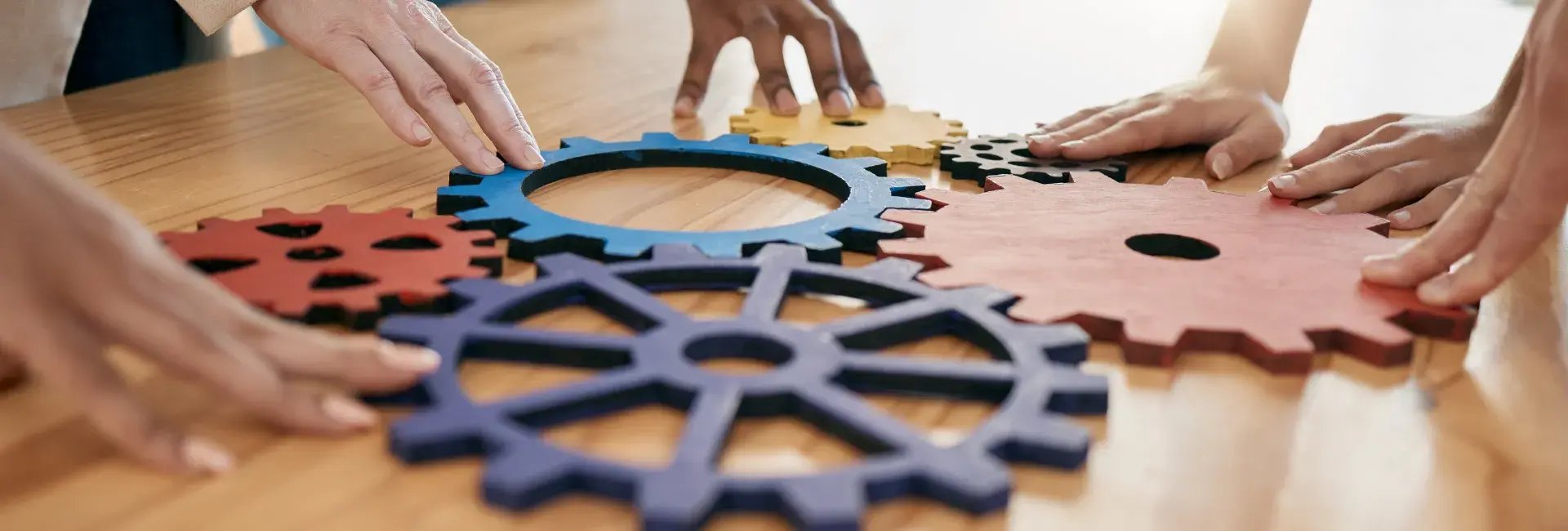 Des mains de personnes diverses plaçant des engrenages en bois colorés sur une table en bois, symbolisant le travail d'équipe et la collaboration.