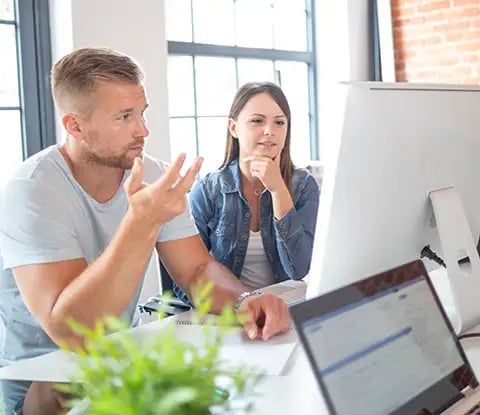 Un groupe discute d'idées dans un espace de travail moderne et lumineux, avec un grand écran, des ordinateurs portables et des plantes sur la table.